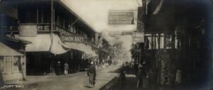 historical black and white photo of a dusty street with shops on both sides, a few pedestrians